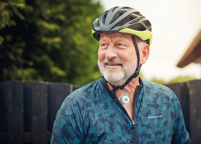 Man wearing a helmet who has a laryngectomy is looking to his right.